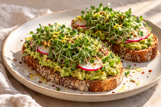 Two slices of avocado toast topped with broccoli microgreens, radish and lemon zest